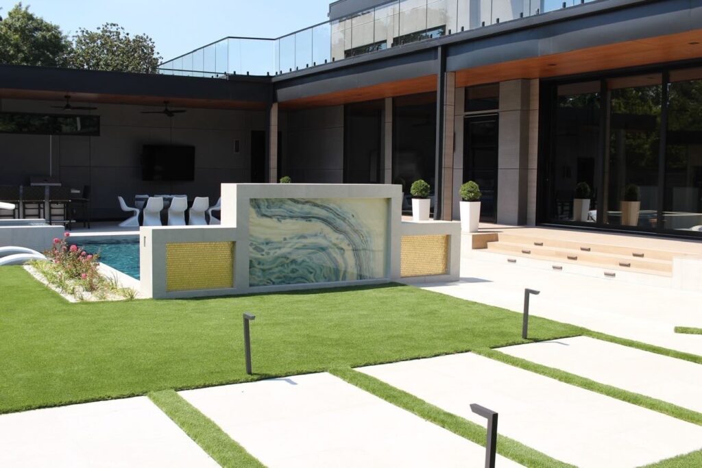 Backlit onyx water wall feature with white concrete deck and artificial turf