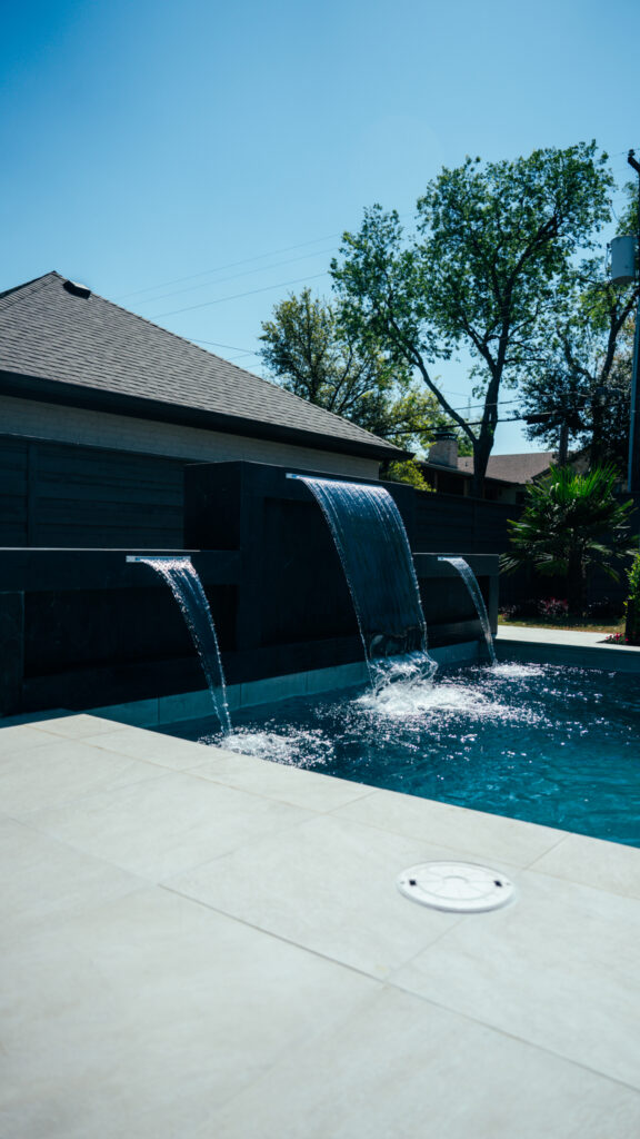 Three sheer descent waterfalls pouring from a dark raised wall into one of our custom pools