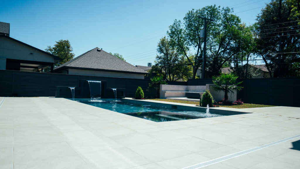 Long geometric pool with white concrete deck and raised wall water features in a modern backyard