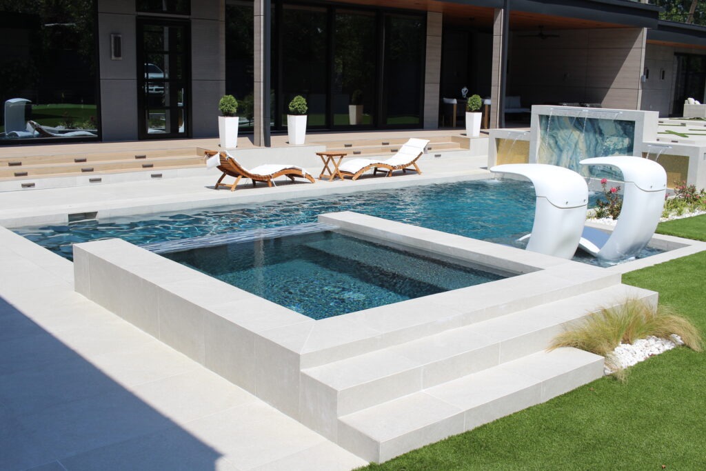 Raised spa and pool with white loungers and a backlit onyx water feature in a finished outdoor living space